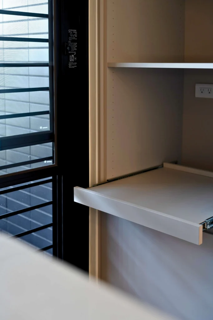 窗邊的廚房電器櫃，中段為可拉出式層板，左側為黑色百葉窗