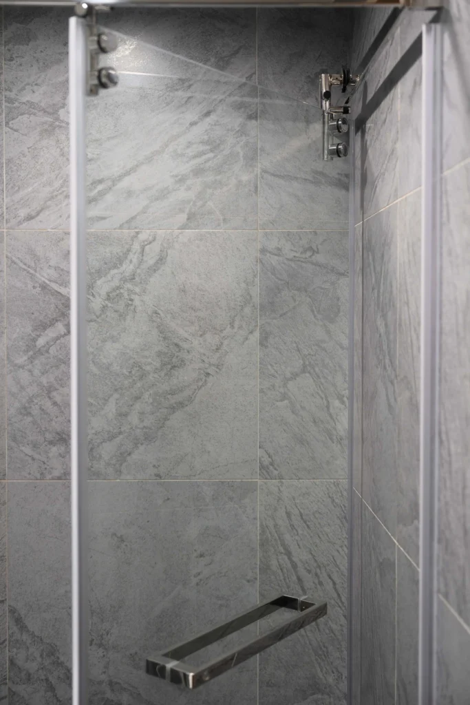 淋浴間灰色石紋牆磚與玻璃隔間，搭配金屬把手與五金